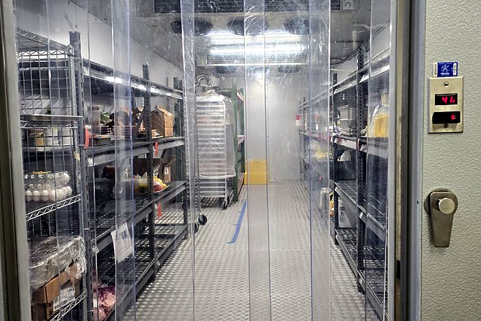Inside the walk-in cooler at Frontier Kitchen Pittsburgh, shelves stocked and a strip curtain at the door.